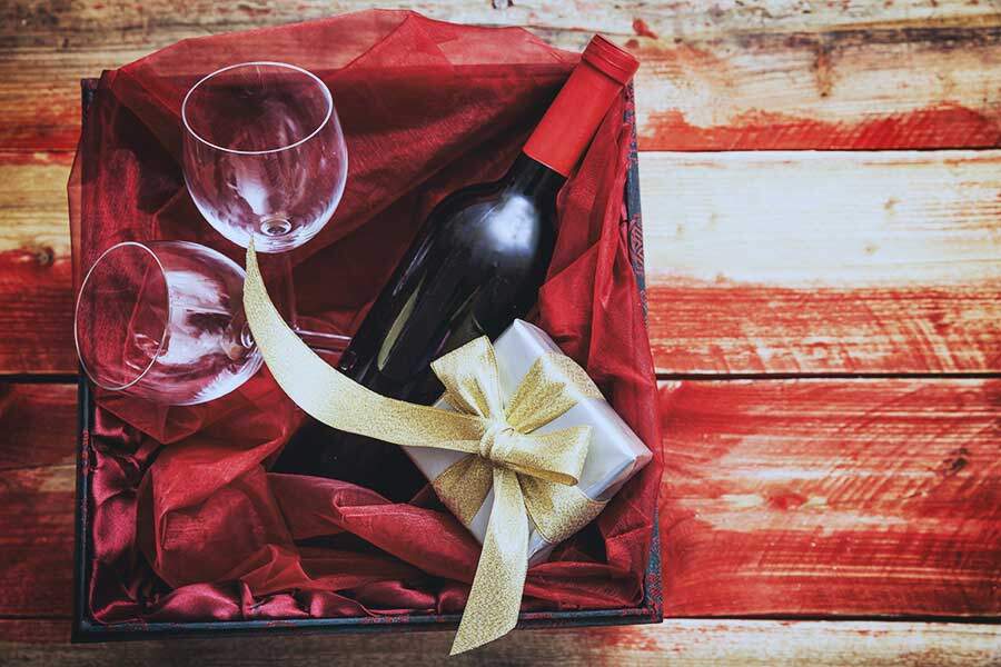 red wine bottle with glasses and a gift in a box and wooden background