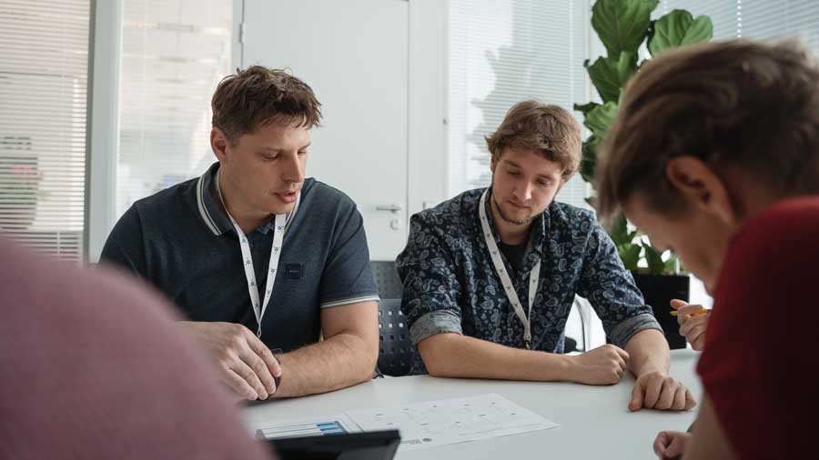 Academic Empowerment for Data Platforms 2 Three men with lanyards sit at a bright conference table, examining a document together in a modern office.